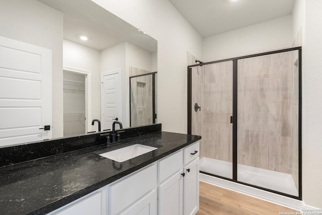 full bathroom featuring recessed lighting, wood finished floors, vanity, a shower stall, and a walk in closet