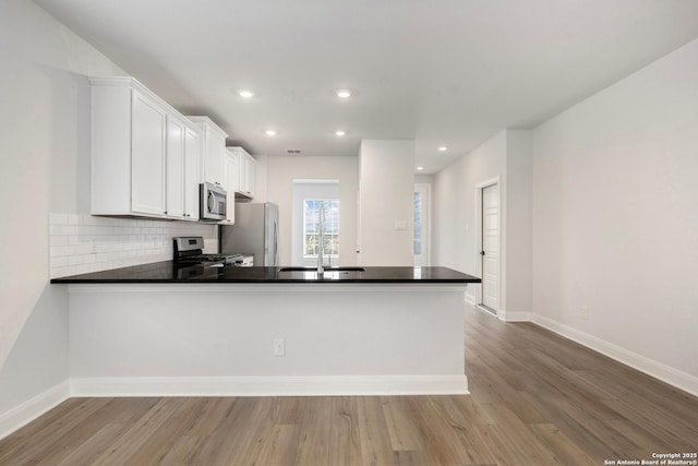 kitchen with stainless steel appliances, dark countertops, a sink, and a peninsula