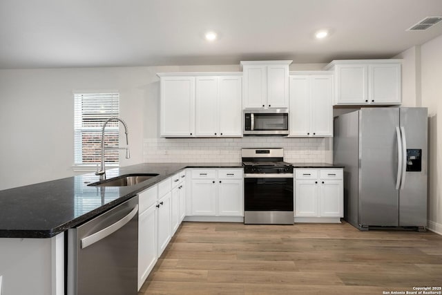 kitchen with appliances with stainless steel finishes, dark stone countertops, a sink, and white cabinetry