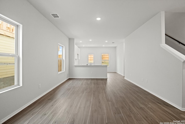 unfurnished living room featuring dark wood-style floors, plenty of natural light, visible vents, and baseboards