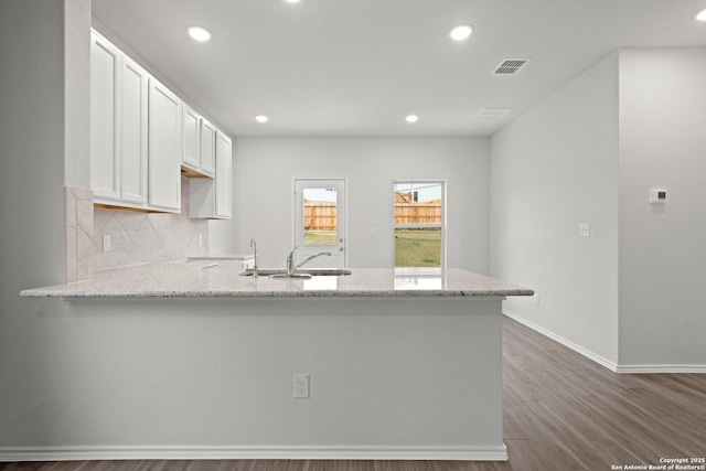 kitchen with tasteful backsplash, visible vents, white cabinetry, light stone countertops, and a peninsula