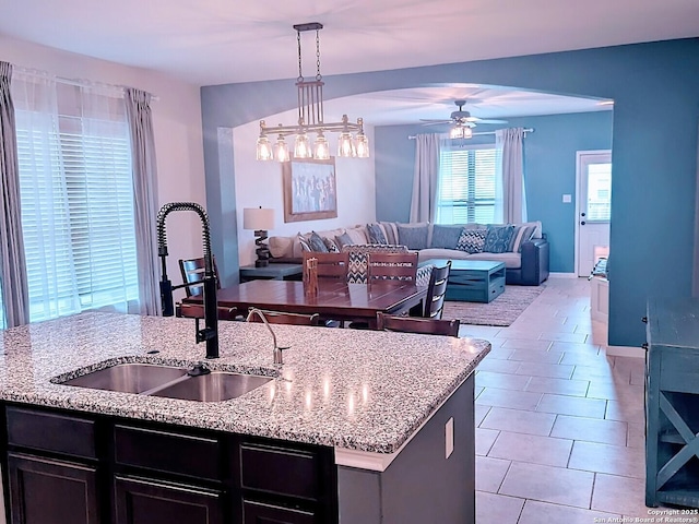 kitchen featuring light stone counters, open floor plan, hanging light fixtures, a kitchen island with sink, and a sink