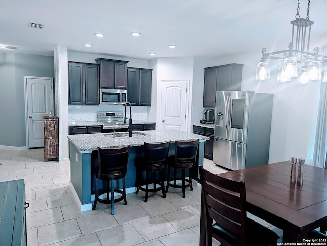 kitchen featuring an island with sink, appliances with stainless steel finishes, a sink, light stone countertops, and backsplash