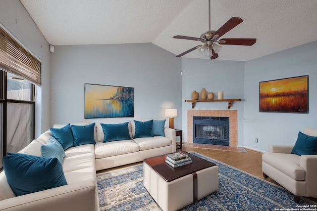 living area featuring a tiled fireplace, ceiling fan, vaulted ceiling, a textured ceiling, and wood finished floors