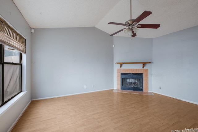 unfurnished living room with light wood finished floors, baseboards, a tile fireplace, lofted ceiling, and a textured ceiling