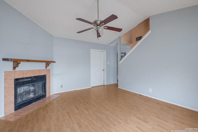 unfurnished living room with baseboards, a ceiling fan, a tiled fireplace, stairs, and light wood-type flooring