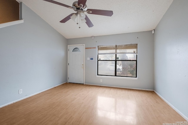 empty room featuring a textured ceiling, light wood-style flooring, a ceiling fan, baseboards, and vaulted ceiling