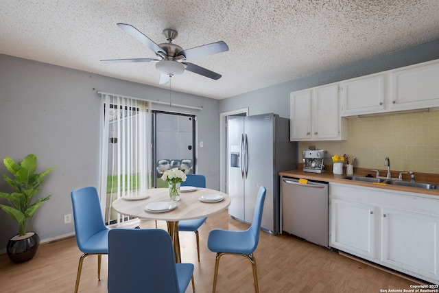 kitchen with stainless steel appliances, backsplash, light wood-style floors, white cabinetry, and a sink