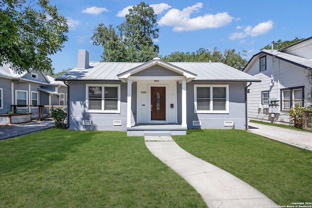 bungalow-style home with a chimney, metal roof, a standing seam roof, and a front yard