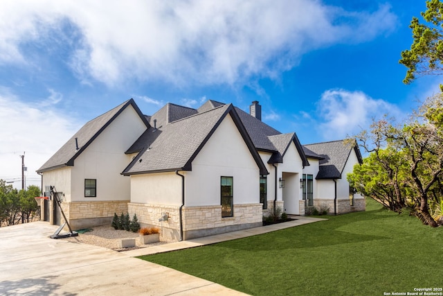 view of side of property with a yard, stone siding, roof with shingles, stucco siding, and a chimney