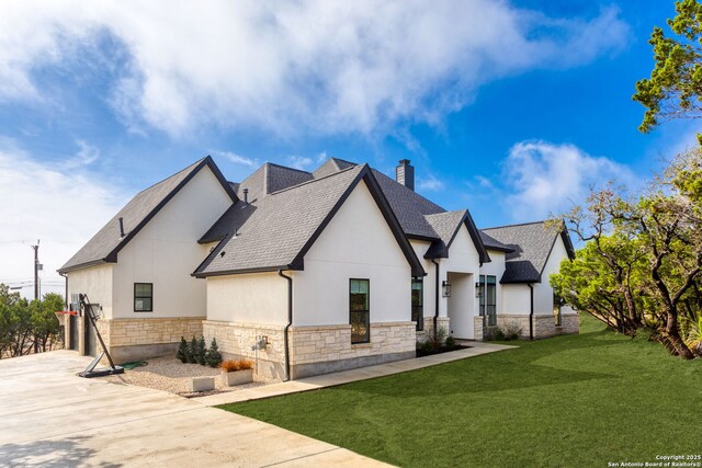 view of side of property with a yard, stone siding, roof with shingles, stucco siding, and a chimney