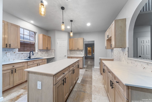 kitchen featuring light brown cabinets, decorative backsplash, a sink, and a center island