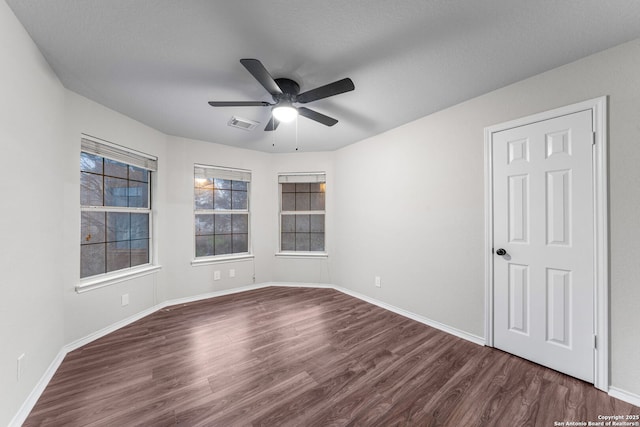 spare room with dark wood-style floors, visible vents, baseboards, and a ceiling fan