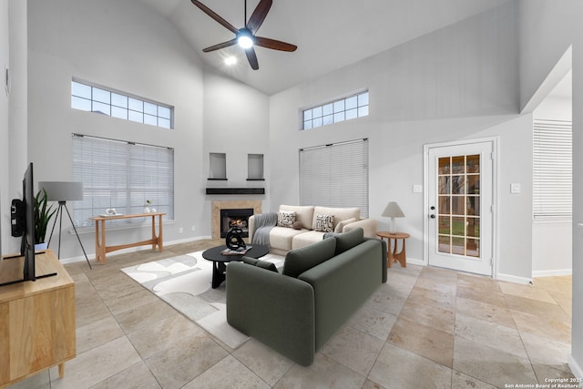 living area with high vaulted ceiling, ceiling fan, a lit fireplace, and baseboards