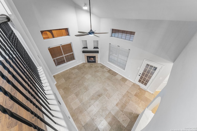 living room with ceiling fan, a fireplace, high vaulted ceiling, and baseboards