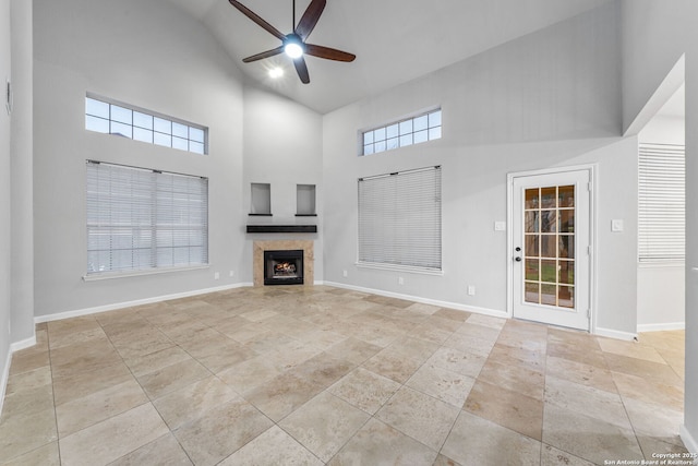 unfurnished living room with high vaulted ceiling, ceiling fan, a lit fireplace, and baseboards