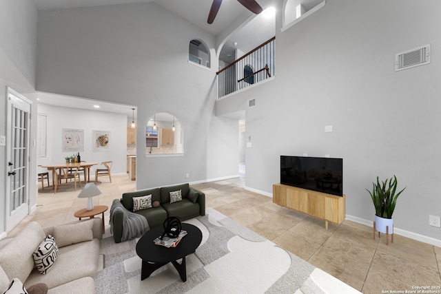 living area with a ceiling fan, arched walkways, visible vents, and baseboards