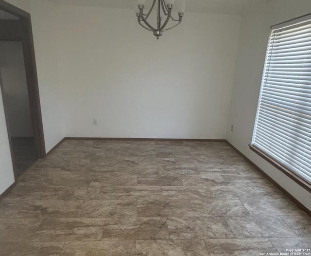 unfurnished room featuring a chandelier, a wealth of natural light, and baseboards