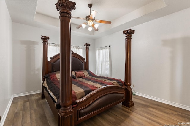 bedroom featuring decorative columns, baseboards, ceiling fan, dark wood-style flooring, and a tray ceiling