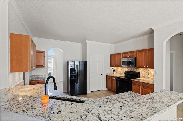 kitchen featuring arched walkways, black appliances, a peninsula, and a sink