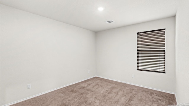 spare room featuring light colored carpet, visible vents, and baseboards