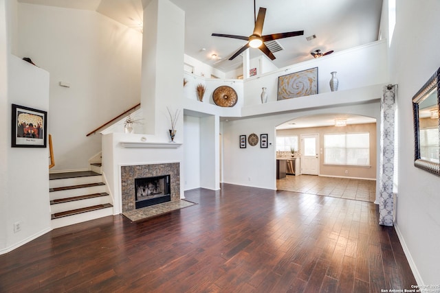 unfurnished living room with arched walkways, a tile fireplace, a towering ceiling, wood finished floors, and stairs