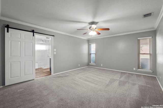 carpeted spare room featuring a barn door, crown molding, visible vents, and a wealth of natural light