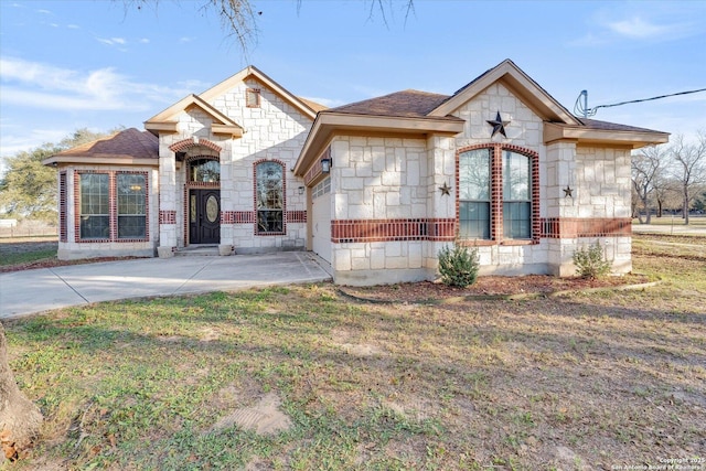 view of front of house featuring stone siding, roof with shingles, a front yard, and driveway