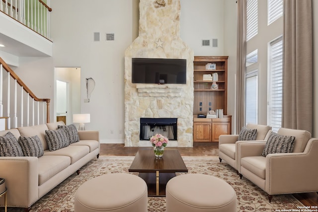 living room with a stone fireplace, visible vents, a towering ceiling, and wood finished floors