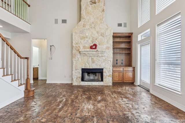 unfurnished living room featuring a stone fireplace, stairway, visible vents, and baseboards