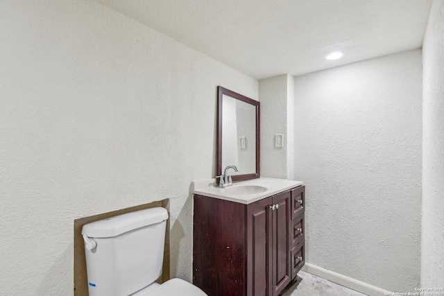 bathroom featuring toilet, a textured wall, vanity, and baseboards