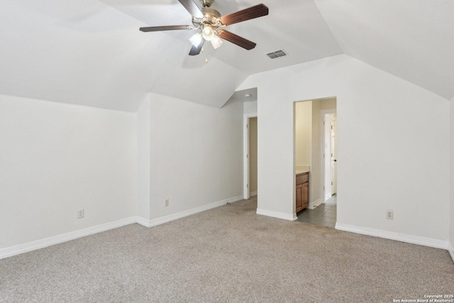 additional living space featuring light colored carpet, visible vents, vaulted ceiling, ceiling fan, and baseboards