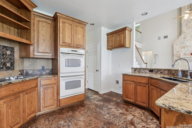 kitchen featuring gas stovetop, brown cabinetry, a sink, and white double oven