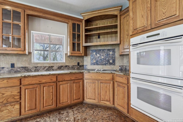 kitchen featuring double oven, glass insert cabinets, light stone counters, and black electric cooktop