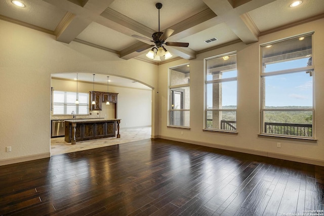 unfurnished living room with arched walkways, dark wood-type flooring, plenty of natural light, and coffered ceiling