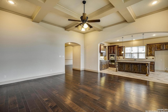 unfurnished living room featuring arched walkways, coffered ceiling, dark wood finished floors, and ceiling fan