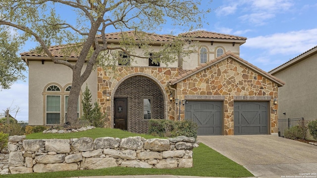 mediterranean / spanish house with a tile roof, stucco siding, concrete driveway, an attached garage, and stone siding