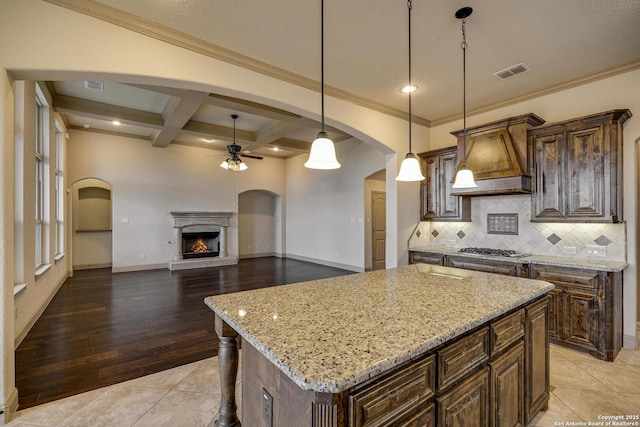 kitchen with visible vents, arched walkways, a kitchen island, decorative light fixtures, and light stone countertops