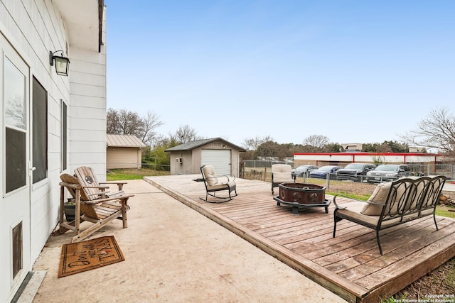 wooden deck with an outdoor fire pit, a detached garage, fence, and an outbuilding