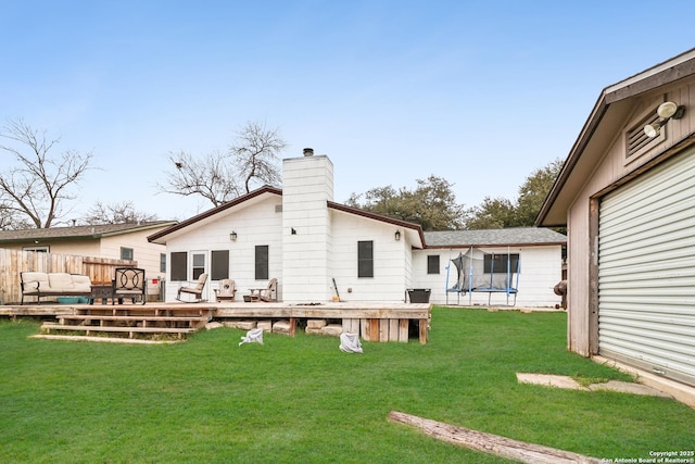 rear view of property featuring a trampoline, a lawn, a chimney, and a wooden deck