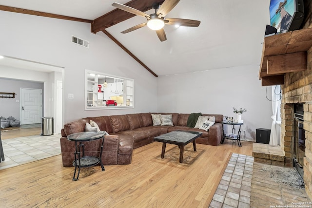 living area with vaulted ceiling with beams, visible vents, a ceiling fan, a brick fireplace, and wood finished floors