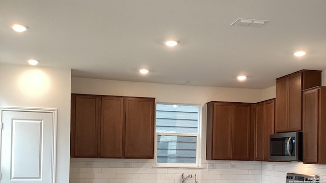 kitchen featuring tasteful backsplash, stainless steel microwave, range, and visible vents