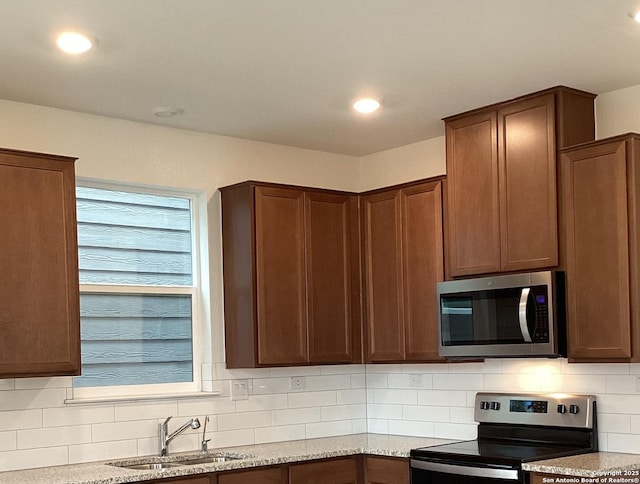 kitchen with light stone counters, stainless steel appliances, recessed lighting, tasteful backsplash, and a sink