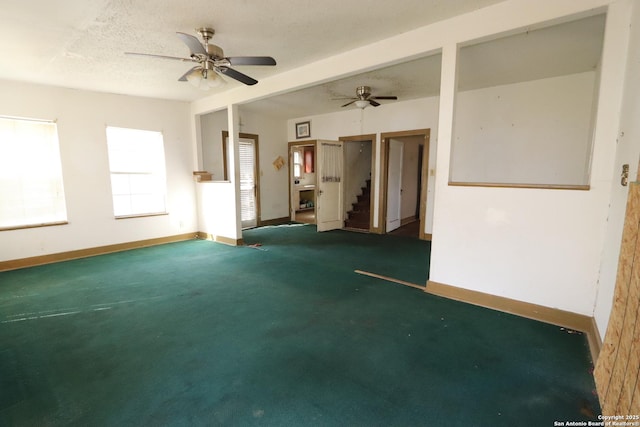 empty room with baseboards, dark carpet, ceiling fan, and a textured ceiling