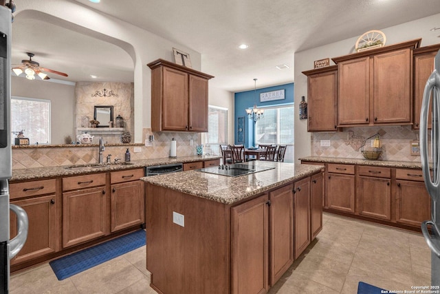 kitchen with brown cabinets, decorative light fixtures, a kitchen island, a sink, and light stone countertops