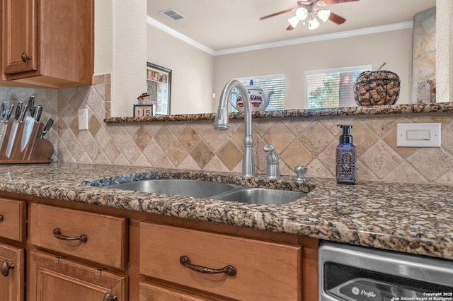 kitchen with brown cabinets, crown molding, visible vents, a sink, and dark stone countertops