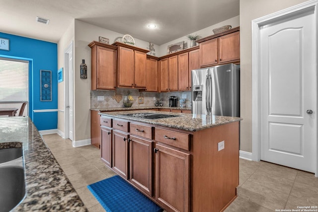 kitchen featuring tasteful backsplash, dark stone counters, stainless steel fridge with ice dispenser, brown cabinets, and a center island