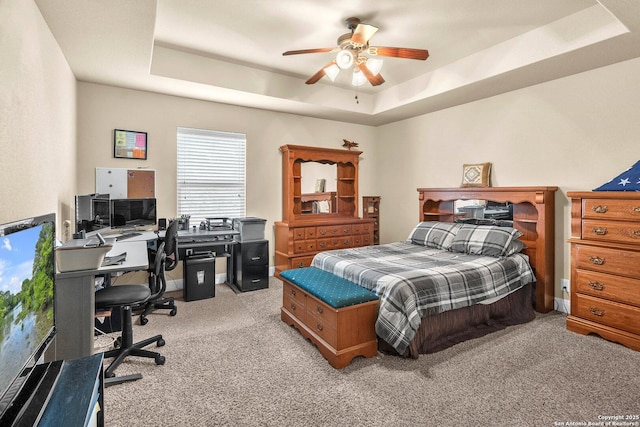 bedroom featuring baseboards, a tray ceiling, a ceiling fan, and light colored carpet