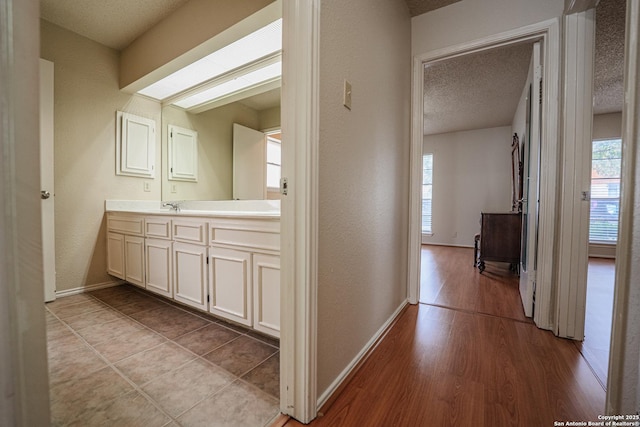 hallway with baseboards, a textured wall, light wood-style flooring, a textured ceiling, and a sink