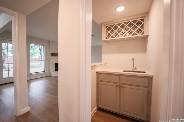 bar with a fireplace, a sink, baseboards, wet bar, and dark wood-style floors